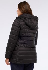 Chaqueta de plumón negra con capucha, con un diseño acolchado, costuras horizontales y una textura suave. Detalles incluyen puños elásticos.