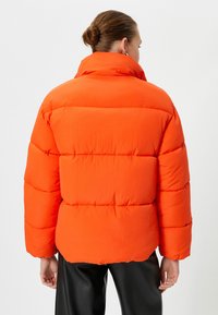 Lys orange pufferjakke med høj krave og kviltet design. Har kraftig polstring og en afslappet pasform. Glat, blank overflade.