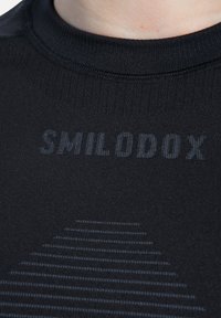 Czarna sportowa koszulka z prążkowanym, okrągłym dekoltem. Na przodzie znajduje się logo "SMILODOX" oraz poziomy wzór w ciemniejszym odcieniu czerni.