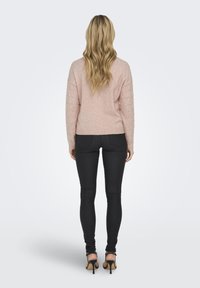 Lichtroze trui met textuur op de mouwen, ribgebreide zoom, gecombineerd met zwarte skinny jeans en zwarte hoge hakken. Zicht vanuit de achterkant.