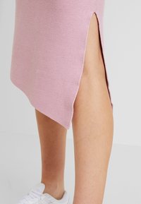 Růžová pletená sukně s bočním rozparkem, s jemnou texturou a mírně asymetrickým lemem. Kombinováno s bílými teniskami.