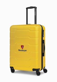 Valigia gialla rigida con superficie textured, zip nera e maniglia, quattro ruote nere e logo Lamborghini nella parte anteriore.