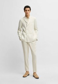 Crème dubbelgeknoopte colberts met notched revers, bijpassende broeken en lichtbruine loafers. Glad materiaal met voorzakken.