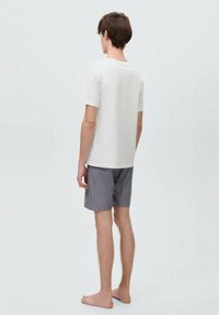 Hvid bomulds T-shirt med kortærmer, parret med mørkeblå og hvide stribede shorts. Modellen er barefodet og står med ryggen til.