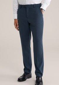 Pantalon de costume bleu marine avec une taille plate, deux poches latérales et une fermeture à un bouton, assorti à des mocassins noirs et une chemise blanche à boutons.