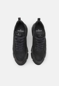 Baskets noires avec une tige en daim et en mesh, dotées de lacets épais, d'un col rembourré et d'une semelle épaisse avec une finition légèrement texturée.