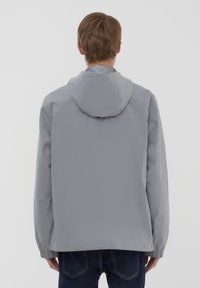 Giacca impermeabile grigia con cappuccio, maniche elastiche e taglio dritto. Texture liscia, senza motivi visibili o dettagli in metallo.