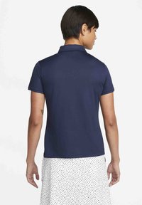 Námořnicky modrá polo košile s límečkem a krátkými rukávy, vyrobená z hladkého materiálu. Má jednoduchý, čistý design.