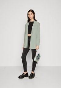 Light green blazer, black crop top, black skinny jeans, and chunky black shoes. Small iridescent handbag with silver chain detail.