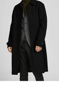 Svart ullblandad kappa med knäppning fram, spridd krage och en lös passform. Bärs över en grå väst och polotröja.