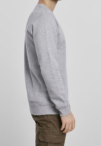 Sudadera gris de manga larga y puños acanalados, hecha de una tela suave, con un cuello redondo y un corte relajado.