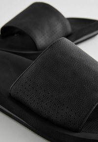 Schwarze Rutschsandalen mit strukturierten synthetischen Riemen, Perforationen im Obermaterial und einer glatten, gepolsterten Innensohle für Komfort.