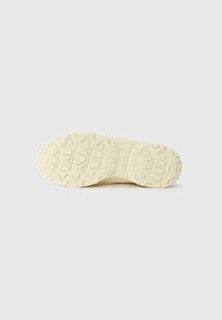 Heledad kreem värvi sneakerite tallad tekstureeritud kummist, millel on geomeetrilised mustrid haardeks ja stabiilsuseks. Sile pind koos peente detailidega.