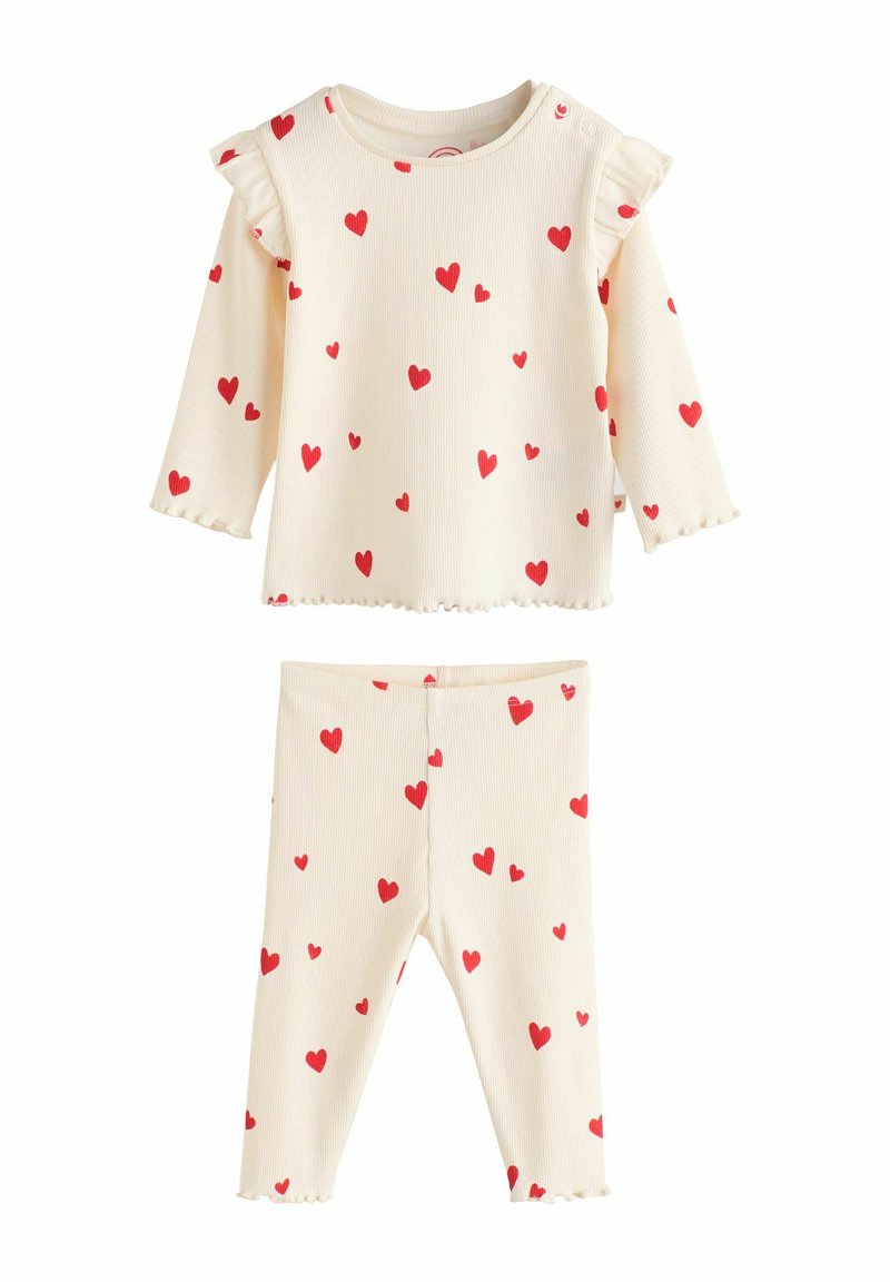 Sada světle krémového dlouhého trička s dlouhým rukávem a legín s červenými srdíčkovými vzory. Tričko má volánkové ramínka a zkosený lem; celá sada má žebrovanou strukturu.