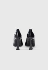 Sorte lærhæl med en blank finish, vinklet stilettohælk, og et slankt, spidst tådesign. Glat tekstur med subtile syninger.