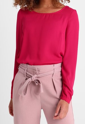 Fuchsia blouse met lange mouwen en een ronde hals, gecombineerd met lichtroze broek met hoge taille en een ceintuur met strikdetail.