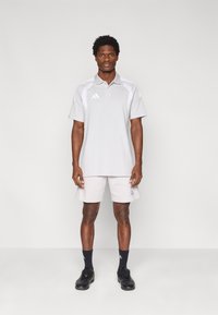 Ανοιχτό γκρι πόλο μπλουζάκι με λευκές λεπτομέρειες, συνδυασμένο με ανοιχτόχρωμο σορτς. Το σύνολο διαθέτει σήμανση Adidas και είναι κατασκευασμένο από λείο, αεριζόμενο ύφασμα.