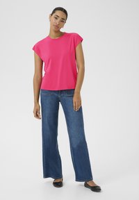 Helles pinkes Kurzarmoberteil mit rundem Ausschnitt, kombiniert mit weiten blauen Jeans aus Denim und schwarzen flachen Schuhen. Glatte Stofftextur.