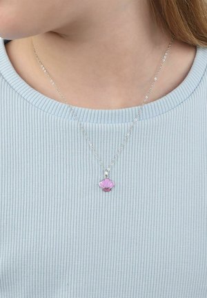 Collier en chaîne argentée avec un pendentif en coquillage rose, porté sur un t-shirt côtelé bleu clair autour du cou et de l'épaule d'une personne.