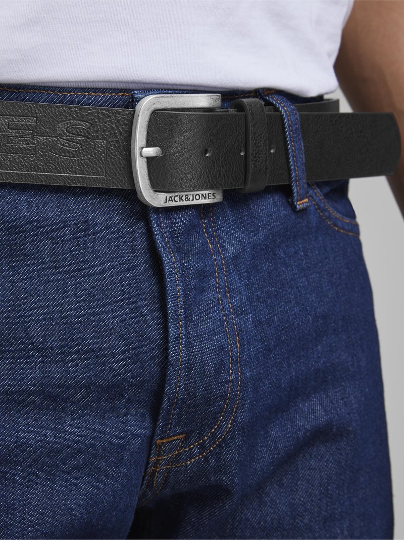 Cinturón de cuero negro texturizado con una hebilla metálica plateada. Presenta el logotipo grabado "JACK&JONES" en la correa, combinado con jeans de denim azul.