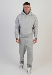 Set di felpa con cappuccio e pantaloni della tuta grigi realizzati in tessuto morbido, con tasca a marsupio e dettaglio con logo. Accompagnato da scarpe da ginnastica bianche.