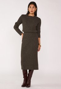 Robe deux pièces en maille côtelée vert foncé avec un crop top ajusté et une jupe midi, présentant une texture douce et des accents métalliques subtils.