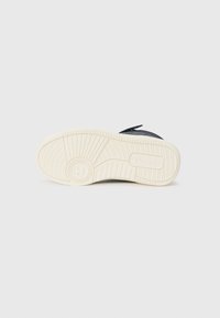 Czarna podeszwa sneakerów z teksturowanym wzorem, kremowa gumowa podeszwa zewnętrzna oraz detal z logo. Zaprojektowane z myślą o przyczepności i trwałości.