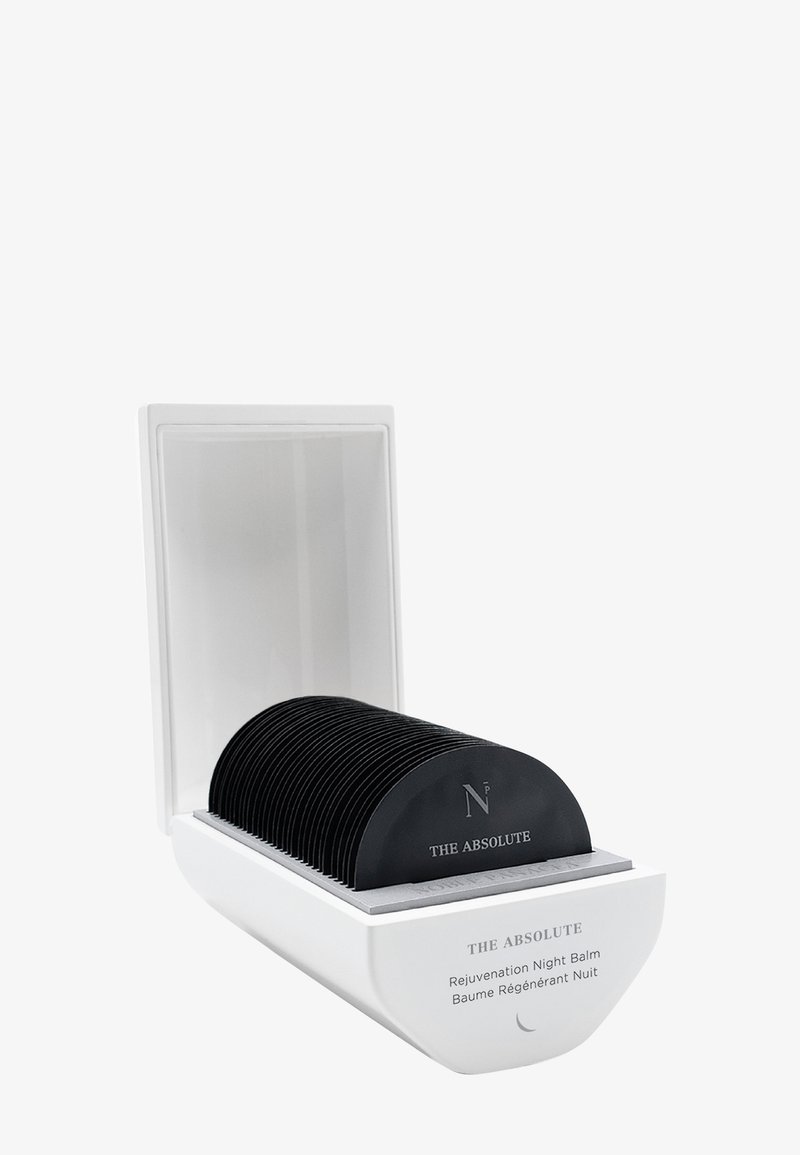 Hvid beholder med åben låg indeholder flere sorte, buede engangsindlæg mærket "THE ABSOLUTE Rejuvenation Night Balm."