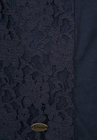 Navy materiał z dzianinowym wzorem w kwiaty o strukturalnym wyglądzie. Na dole przymocowana jest mała brązowa metka z napisem 'Denim'.