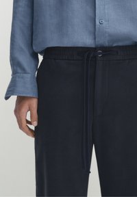 Marine joggers met een elastische tailleband en trekkoord, gecombineerd met een lichtblauw overhemd met knopen, dat een textuurstof toont.