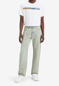 Bílá tričko s logem "LEVI'S" a barevnými pruhy, kombinované s světlými rovnými džínami a bílými teniskami.
