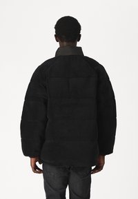 Czarna polarowa kurtka z wysokim kołnierzem, w oversize'owym kroju i pikowanymi sekcjami. Widać teksturowany materiał i obniżone szwy ramion.