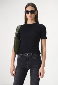 T-shirt noir ajusté, à manches courtes, associé à un jean foncé. Sac à épaule vert olive au design structuré. Lunettes de soleil noires.