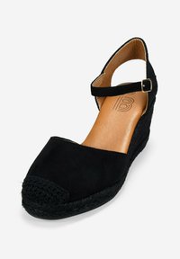 Espadrillas nere a cuneo con tomaia in suede, punta tonda, cinturino alla caviglia con fibbia dorata e suola in juta intrecciata. Sottopiede in pelle liscia.