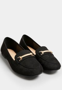 Mocassini in suede neri con accento di catena dorata, punta arrotondata e suola piatta. Il design presenta un dettaglio di cuciture sulla parte superiore.