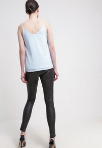 Top sin mangas de color azul claro con un diseño de espalda en V, combinado con pantalones de cuero negro ajustados y zapatos de tacón negro.