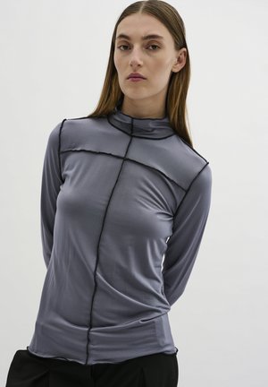 Grijze langarmtop met een mock neck, voorzien van zwarte contrasterende stiksels en een getailleerd ontwerp. Gladde textuur met minimale naden.