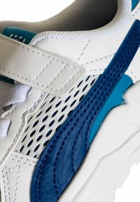 Sneaker bianca con accenti blu, caratterizzata da una tomaia sintetica testurizzata, pannelli in mesh e chiusura a strappo. Design a profilo basso.