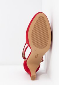 Chaussure à talon aigu en suède rouge avec un bout pointu, une sangle arrière et une semelle en caoutchouc beige texturé. Fini lisse avec des accents minimaux.