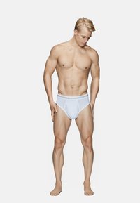 Hvide bomuldsbriefs med et mærket elastikbånd, der har en tætsiddende pasform og en glat tekstur. Modellen har en slank, muskuløs kropsbygning.