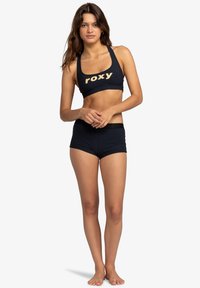 Zwart sportief bikini set bestaande uit een crop top met "roxy" in lichtgoud gedrukt en bijpassende hoge shorts met een zwarte band.
