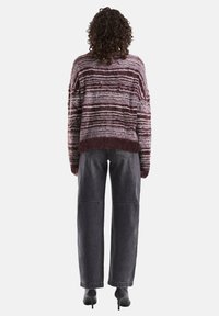 Burgunder- und cremefarbener gestreifter kuscheliger Pullover mit cropped Schnitt, kombiniert mit hochgeschnittenen grauen Jeans und schwarzen Absätzen.