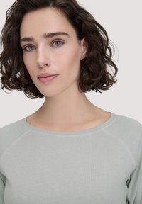 Hellgrünes, langärmeliges Oberteil mit Rundhalsausschnitt und Raglanärmeln, aus weichem, glattem Stoff gefertigt. Schlichtes Design, ohne Muster oder Akzente.