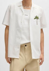 Witte short-sleeve shirt van lichtgewicht katoen, met een palmboomgraphic op de linkerborst. Gecombineerd met een simpele witte tanktop.