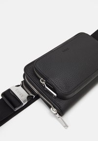 Svart lær crossbody-veske med teksturfinisher, dobbel glidelåsrom, sølvfarget maskinvare og justerbar stropp med metallbuckle.