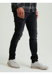 Jeans neri slim-fit con una leggera texture sfumata, abbinati a sneakers chiare con un design a strati e suola in gomma marrone.