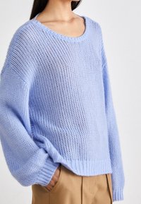 Ljusblå stickad tröja med en lös passform, bred båturringning och ribbad nederkant. Har långa ärmar och en öppen, luftig struktur.