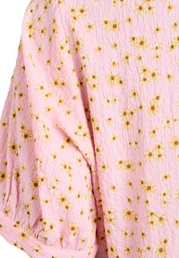 Roze gestructureerde stof met kleine gele en bruine madeliefjesprint, geplooid bij de naden waardoor zachte plooien en volume ontstaan.