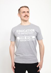Camiseta de algodón gris con un atrevido texto en blanco: "LA EDUCACIÓN ES IMPORTANTE PERO EL GIMNASIO ES MÁS IMPORTANTE". Manga corta y cuello redondo.