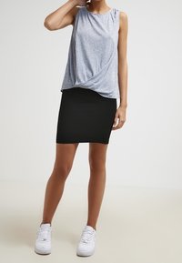 Šedý top bez rukávů s uzlovým designem, spárovaný s těsnou černou strukturovanou tužkovou sukní a bílými teniskami. Hladká textura látky po celé ploše.